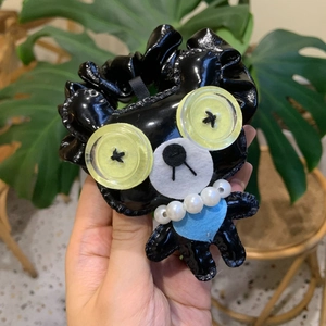 Détail d'un accessoire ours en cuir synthétique noir avec yeux boutons jaunes et perles