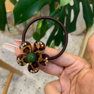 Detailed view of a leopard print flower hair tie with rhinestones and a green bead accent