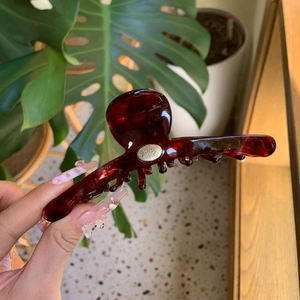 Détail d'une pince à cheveux en acétate rouge foncé avec logo doré Paris Tosca