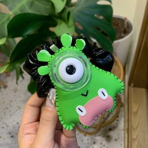 Détail d'un chouchou monstre en cuir vert avec un œil surdimensionné et des lèvres roses