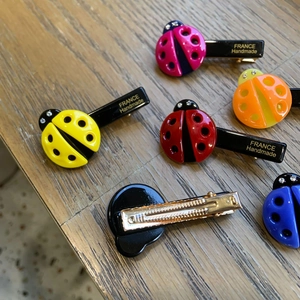 Detail showing ladybug hair clips with vibrant resin colors and gold metal duckbill clips