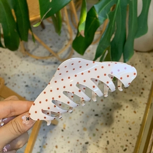 Close-up of white acrylic hair claw with red polka dots and interlocking teeth design