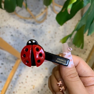 Close-up of a handmade red ladybug hair clip with black spots and France engraving