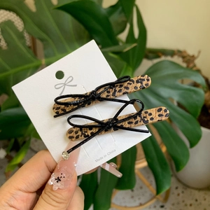 Set of two leopard print hair clips with black bows on a white display card