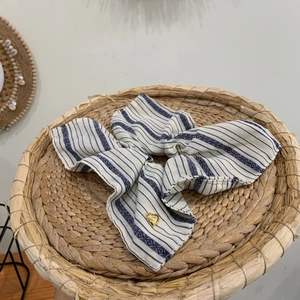 Striped boho hair scrunchie with blue ribbons and a gold heart pendant on a woven tray