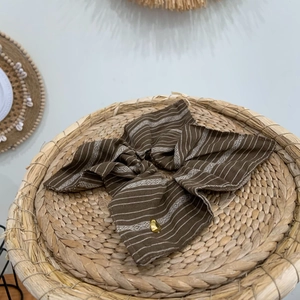 Brown striped oversized scrunchie with a gold heart charm on a woven natural tray
