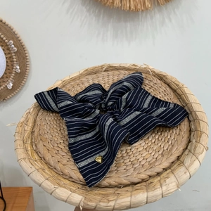 Premium navy striped scrunchie with gold heart pendant on rustic woven tray