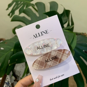 Floral and checkered hair clips set with Alline logo shown on display card with greenery