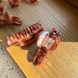 Detail of red and brown plaid hair claw clips on a wooden surface under natural sunlight