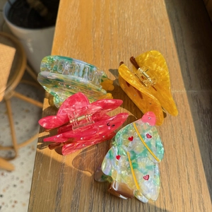 Detailed close-up of four assorted colorful acetate hair claws on a rustic wooden surface
