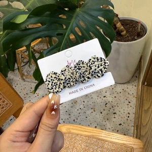 Détail de la pince à cheveux en forme de coquillage à pois noirs et blancs à la main