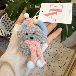Detalle de un colgante de perro tejido a mano con bufanda rosa y etiqueta de marca