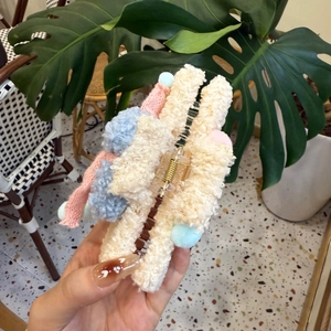 Detalle de una pinza para el pelo de felpa beige con pompones rosas y azules y muelle dorado