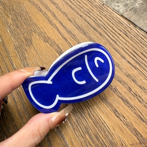 Close-up of a blue acrylic fish-shaped hair claw clip with white outline on wood surface