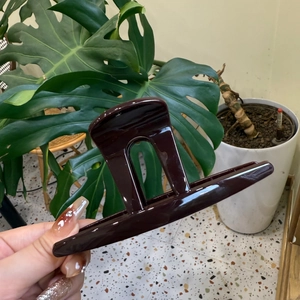 Détail d'une grande pince à cheveux marron café brillant avec une découpe élégante en U
