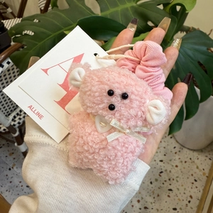 Detailed view of plush pink bear hair scrunchie featuring white ribbon and heart button