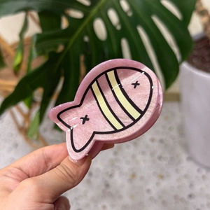 Detailed view of a glittery pink fish hair claw with yellow stripes and stars