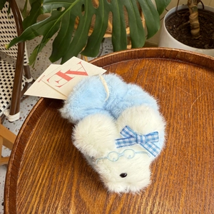 Detail eines flauschigen weißen Hunde-Scrunchies mit Stickerei auf einem Holzteller
