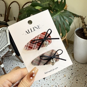 Red and grey plaid bow hair clips with heart charms on card display in hand