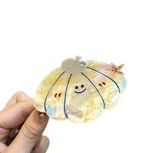 Scallop shell hair claw clip in creamy marble acetate with a smiling face and pink star