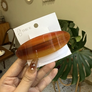 Elegant amber tortoiseshell acetate oval hair clip on a minimalist white paper display card