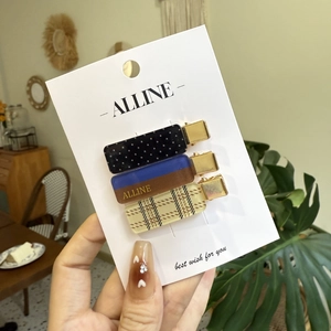 Three-piece set of stylish hair clips featuring polka dots, plaid, and brand logos on gold metal