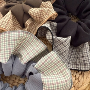 Detail of plaid and solid fabric scrunchies in brown, black, and blue on a straw mat