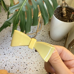 Detail shot of a minimalist light yellow bow hair clip with smooth glossy finish