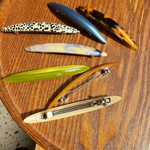 Vue de dessus de six barrettes à cheveux en acétate colorées sur un plateau en bois