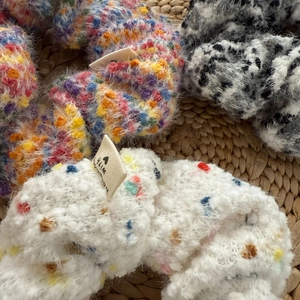Close-up of soft knit fuzzy hair scrunchies with colorful dot patterns on straw mat