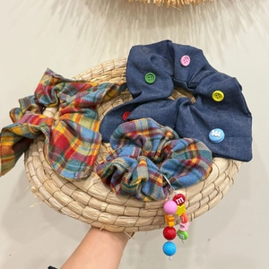 Close-up of three scrunchies with colorful buttons and letter charms in a straw tray