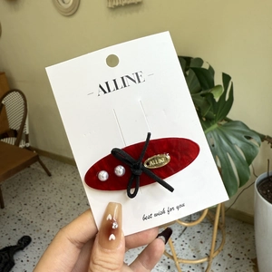 Red oval hair clip with pearls and black bow on a white display card for styling