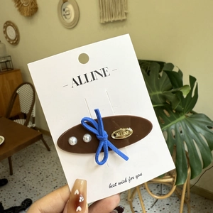 Brown acetate hair clip with blue bow and pearls on a white brand display card