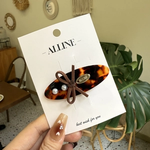 Detail view of tortoiseshell acetate hair clip with suede bow, pearls, and golden tag