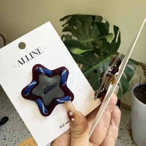 Détail d'une pince à cheveux étoile violette avec corde tissée bleue et blanche sur carte