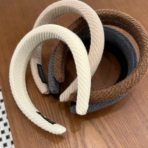 Close-up of four knitted headbands in cream, beige, brown and grey on a wooden table
