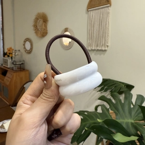 Detail showing high-elastic hair tie with glossy white resin oval rings and brown cord