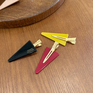 Three minimalist triangular hair clips in black, yellow, and red on a wood surface