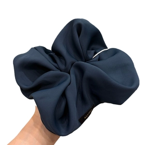 Deep blue textured silk scrunchie with a gold label shown held in hand on white background