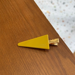 Bright yellow triangle hair clip with France Handmade text on dark wood background