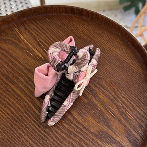 Vue de dessus d'une pince à cheveux à carreaux roses avec nœud sur plateau en bois