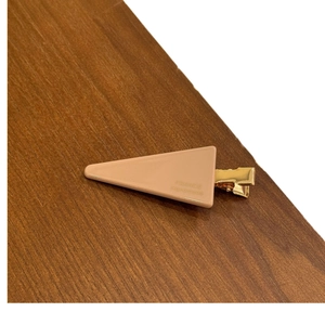 Minimalist light brown triangle hair clip with gold metal base on wooden background