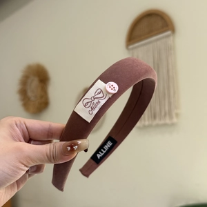 Détail d'un bandeau en tissu marron avec bouton strass rose et étiquette de marque tissée