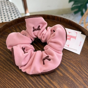 Gros plan d'un chouchou en tissu rose avec broderie de nœuds marrons sur plateau