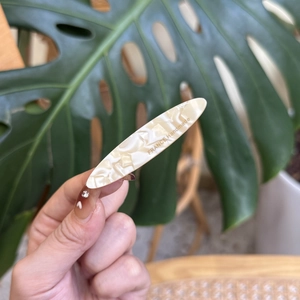 Barrette à cheveux élégante en acétate marbré crème avec logo doré tenue à la main