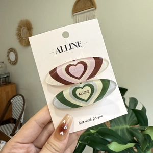 Set of two heart pattern oval hair clips in pink and green on a white display card