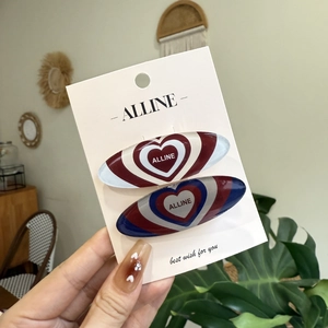 Pair of oval resin hair clips with heart patterns and lettering on a display card