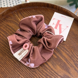 Vue détaillée d'un chouchou floral avec bouton rose et étiquette sur plateau bois