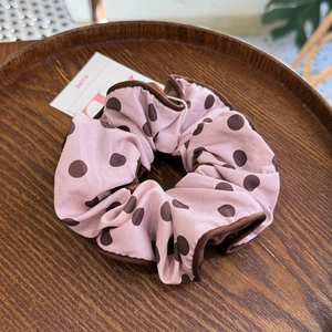 Chouchou en satin rose à pois marrons et liseré de soie sur un plateau en bois