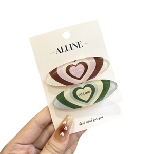 Set of two colorful oval hair clips with concentric heart patterns and Alline logo